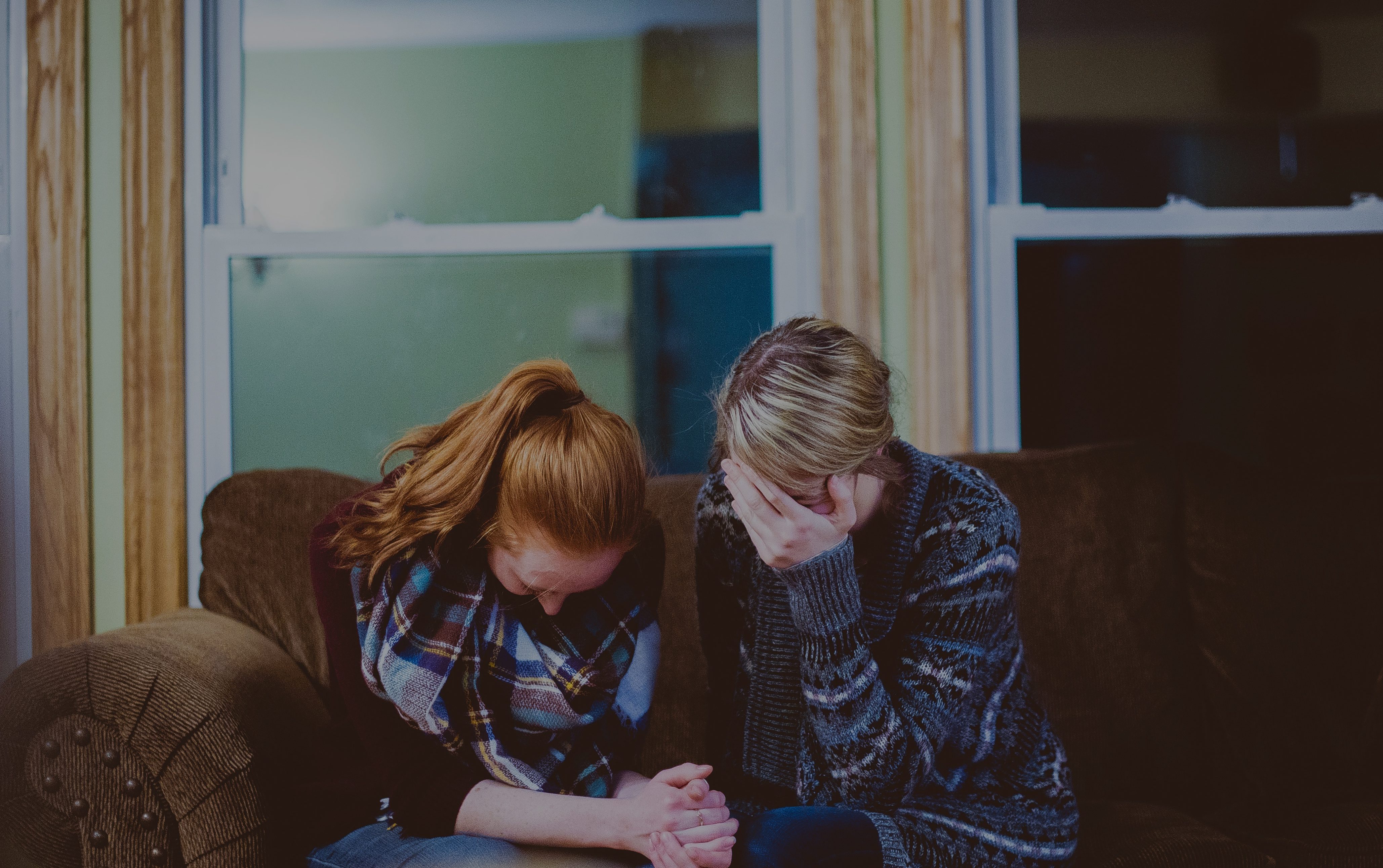 Två ledsna kvinnor sitter i en soffa. Kanske gråter de.