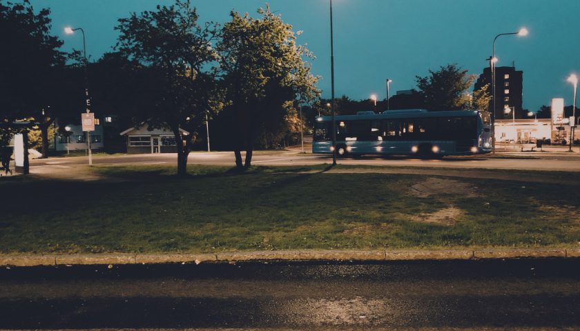 Blå buss kör förbi gräsyta på kvällen