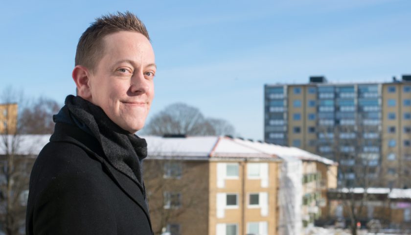 Håkan Eriksson står snett mot kameran och ler. I bakgrunden syns höghus.